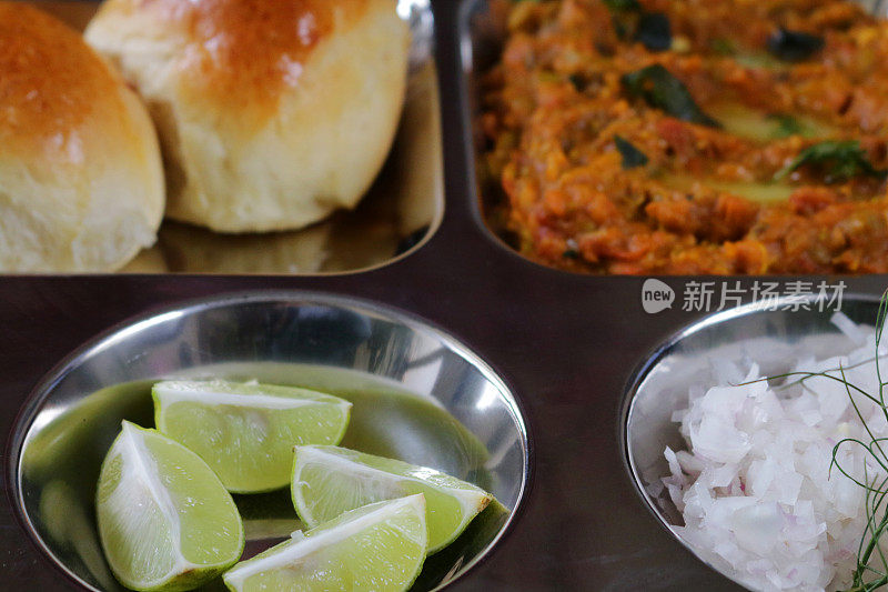 传统的印度/孟买食物Pav bhaji和新鲜出炉的面包卷一起放在不锈钢盘里。Bhaji /肉汁配上切碎的生洋葱、柠檬片和黄油